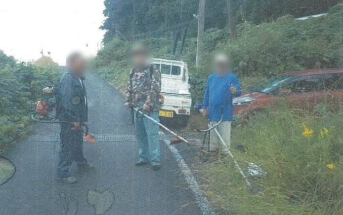 草刈り機を持って道路沿いに立つ地域の方々